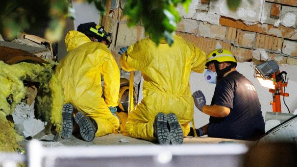 <p>THW-Helfer in Schutzkleidung räumen Trümmer beiseite, um an den letzten noch verschüttetenToten zu gelangen.</p>