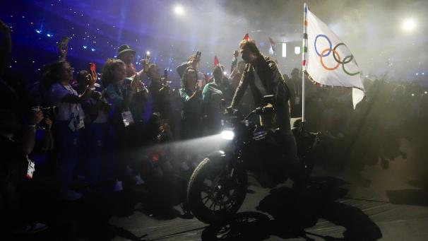 <p>Tom Cruise fährt auf einem Motorrad mit der olympischen Flagge während der Abschlussfeier der Olympischen Sommerspiele 2024 im Stade de France.</p>