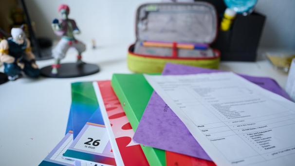 <p>Neue Schulhefte, Ordner und eine Materialliste für das neue Schuljahr liegen auf einem Kinderschreibtisch.</p>