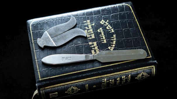 <p>Beschneidungsbesteck, ein Messer und ein Vorhautschutz, liegen auf einem jüdischen Gebetbuch.</p>