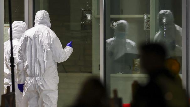 <p>Polizeibeamte der Spurensicherung in weißen Schutzanzügen untersuchen Löcher in Glasscheiben des Kinos.</p>
