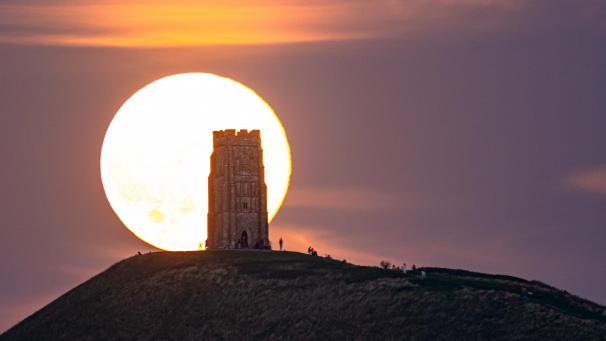 <p>Menschen versammeln sich, während der Supermond über dem St. Michael's Tower auf dem Glastonbury Tor aufgeht.</p>