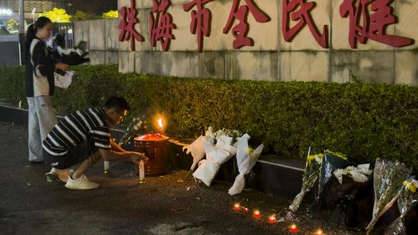 <p>Ein Mann zündet eine Kerze neben Blumen an, die vor dem „Zhuhai People's Fitness Plaza“ aufgestellt wurden.</p>