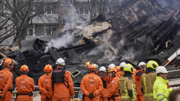<p>Feuerwehrleute stehen vor einem zerstörten Gebäude am Ort einer Explosion, bei der mehrere Wohnungen zerstört und mehrere Menschen verletzt wurden.</p>