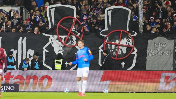 <p>Banner im Kieler Fanblock zeigen die Gesichter von Oliver Mintzlaff und Jürgen Klopp mit einem Fadenkreuz darüber.</p>