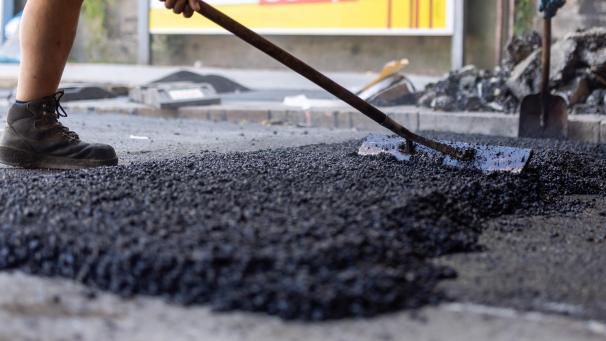 <p>Mitarbeiter eines Straßenbau-Unternehmens verteilen frischen Asphalt auf einer Fahrbahn.</p>