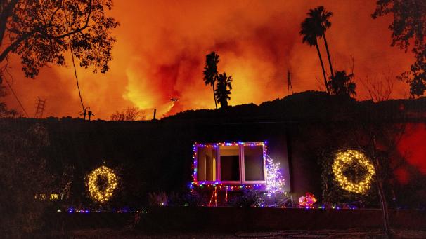 <p>Ein Hubschrauber wirft Wasser auf das Palisades-Feuer hinter einem Haus mit Weihnachtsbeleuchtung im Mandeville Canyon ab.</p>