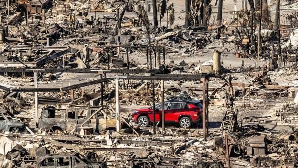 <p>Ein rotes Auto fährt an Häusern und Fahrzeugen vorbei, die durch das Palisades-Feuer in den Pacific Palisades Bowl Mobile Estates zerstört wurden.</p>