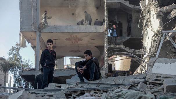 <p>Nach einem israelischen Luftangriff im Flüchtlingsviertel al-Nuseirat im zentralen Abschnitt des Gazastreifens sitzen Menschen vor einem zerstörten Gebäude.</p>