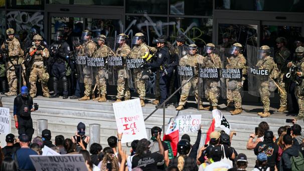 <p>Menschen protestieren in Downtown LA, während Einsatzkräfte der Nationalgarde vor einem Regierungsgebäude stehen.</p>