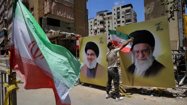 <p>Ein Hisbollah-Anhänger schmückt ein Porträt des Obersten Führers des Iran, Ayatollah Ali Khamenei, mit iranischen Flaggen in einem südlichen Vorort von Beirut während einer Kundgebung, bei der der israelische Angriff auf den Iran und Drohungen gegen den iranischen Führer verurteilt wurden</p>