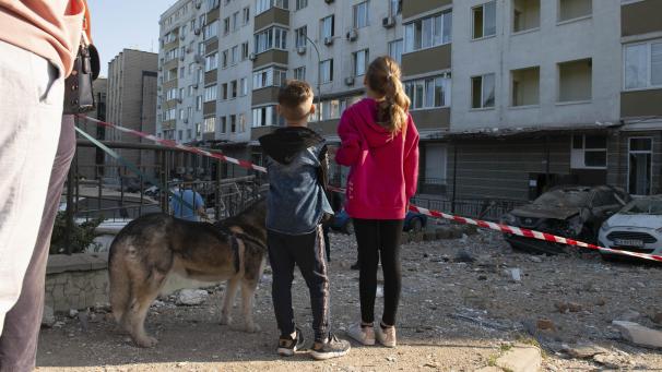 <p>Kinder blicken im Mai 2023 auf stark beschädigte Gebäude, die bei dem dritten russischen Luftangriff auf die ukrainische Hauptstadt innerhalb der letzten 24 Stunden beschädigt wurden.</p>