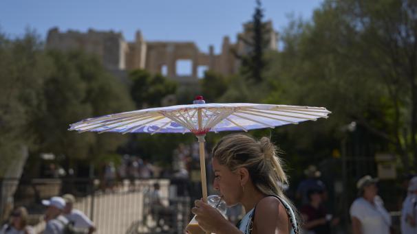 <p>Eine Touristin mit einem Sonnenschirm steht auf der Akropolis.</p>
