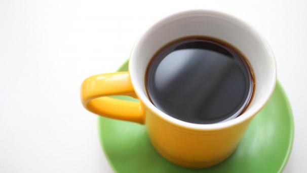 <p>Eine gelbe Tasse mit schwarzem Kaffee steht auf einem Tisch.</p>