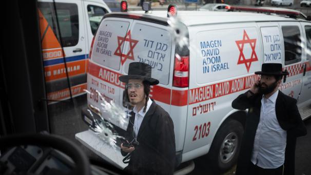 <p>Ein israelischer Mann betrachtet Einschusslöchter in der Windschutzscheibe eines Busses nach einem Anschlag an einer Bushaltestelle - hinter ihm steht ein Fahrzeug des israelischen Rettungsdienstes Magen David Adom.</p>