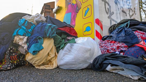 <p>Gebrauchte Kleidungsstücke liegen vor einem Sammelcontainer für Altkleider.</p>