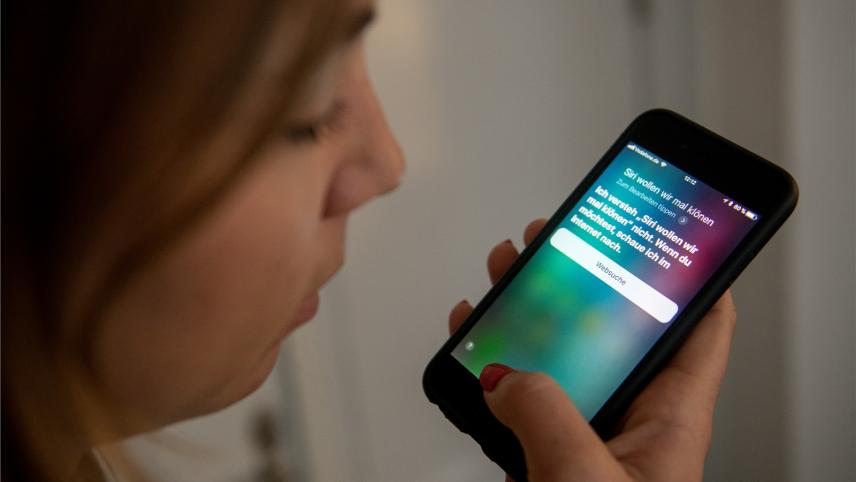<p>Eine junge Frau bedient auf einem iPhone die Spracherkennung des Apple-Programms Siri.</p>