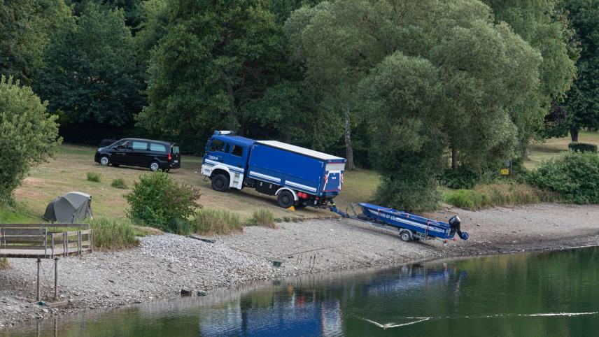 <p>Ein Leichenwagen und ein Fahrzeug mit Boot des Technischen Hilfswerks (THW) stehen am Eiserbachsee.</p>
